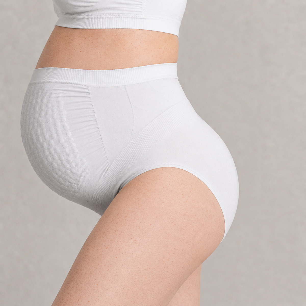 White high-waisted stretch mark prevention pregnancy underwear worn by a pregnant modelon a neutral background 